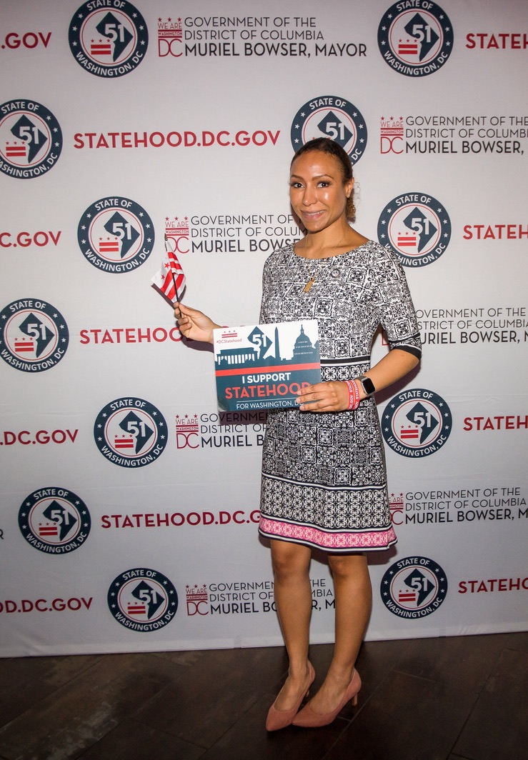 Rachel Williams for DC Statehood standing in front of Statehood.DC.Gov step-and-repeat red white and blue banner